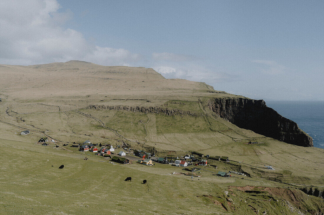 Village on grassy, sunny cliff, Mykines, Faroe Islands\n