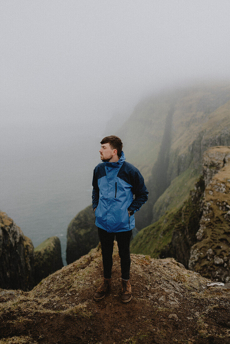 Man in jacket hiking on rugged cliff sea stacks, Dunnesdrangar, Vagar, Faroe Islands\n