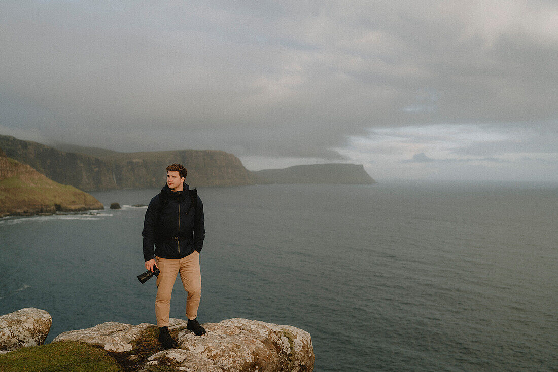 Wanderer mit Kamera am Rande einer Klippe über dem Meer, Neist Point, Isle of Skye, Schottland