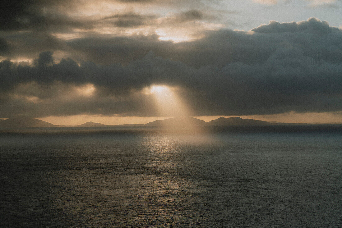 Sonnenstrahl in bewölktem dramatischen Himmel über dem Meer bei Sonnenuntergang, Neist Point, Isle of Skye, Schottland