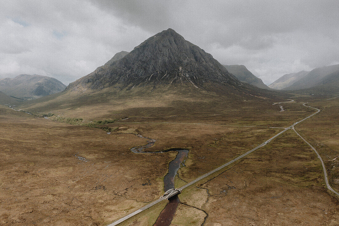 Panoramablick auf Straße und Fluss unterhalb der majestätischen Berglandschaft, Glencoe, Schottische Highlands, Schottland