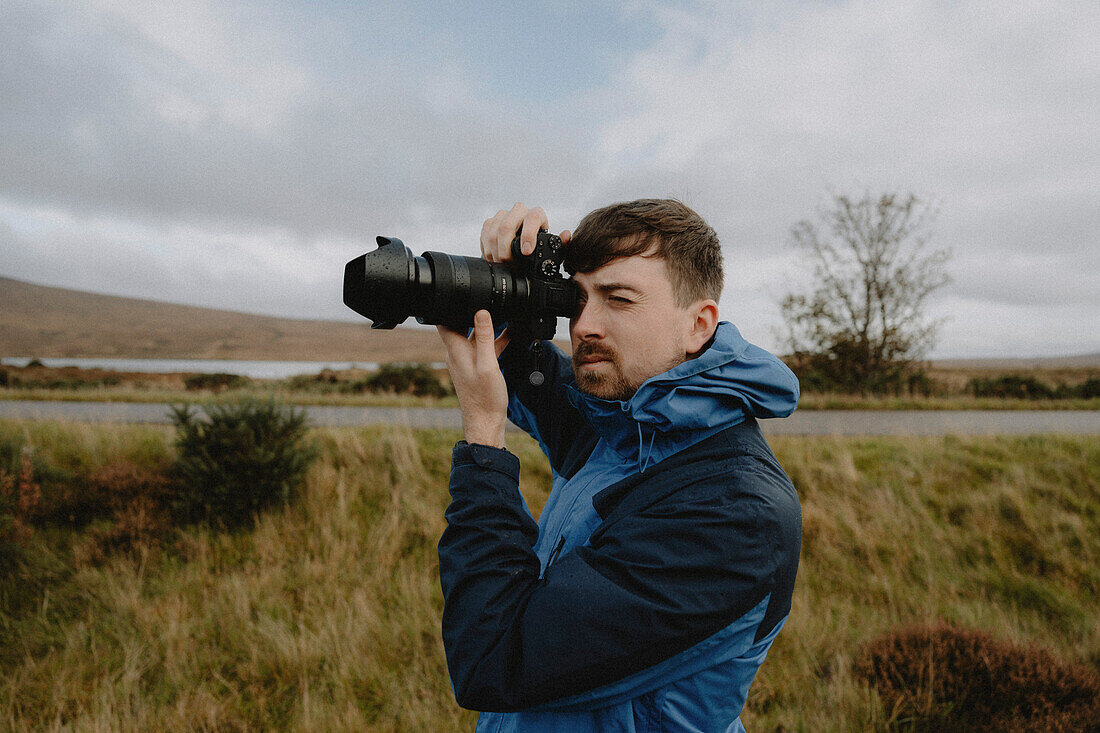 Männlicher Fotograf mit Spiegelreflexkamera auf grasbewachsenem Feld, Durness, Schottische Highlands, Schottland