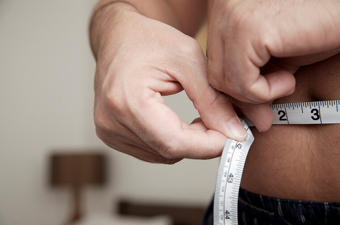 Close up of man measuring waist with tape measure\n