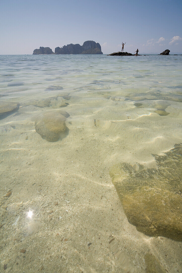 Nahaufnahme von kristallklarem Meerwasser mit auf Felsen stehenden Frauen, Koh Phi Phi, Thailand