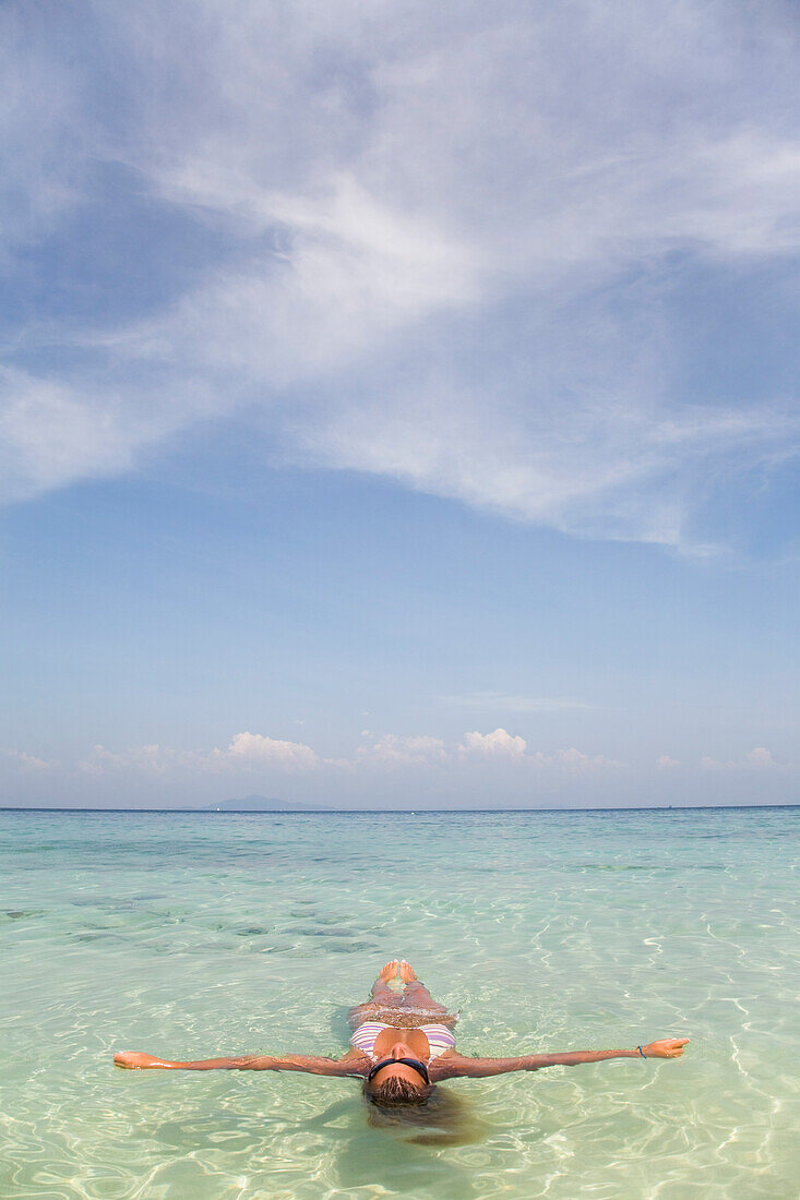 Junge Frau schwimmt mit ausgebreiteten Armen im kristallklaren Meerwasser, Koh Phi Phi, Thailand