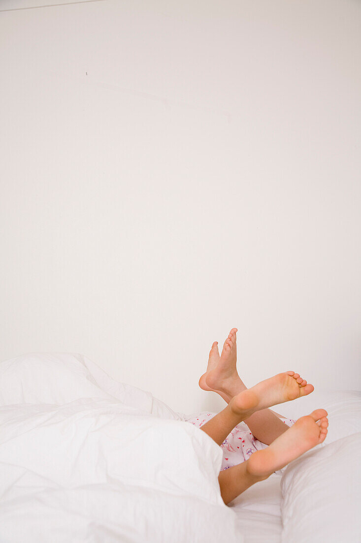 Zwei Paar Füße kommen aus einer weißen Bettdecke