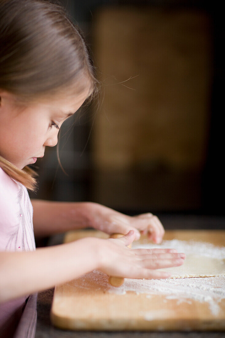 Young girl rolling dough on table\n