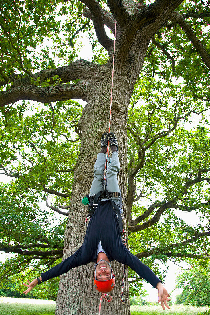 Portrait of a climber hanging upside down from tree\n