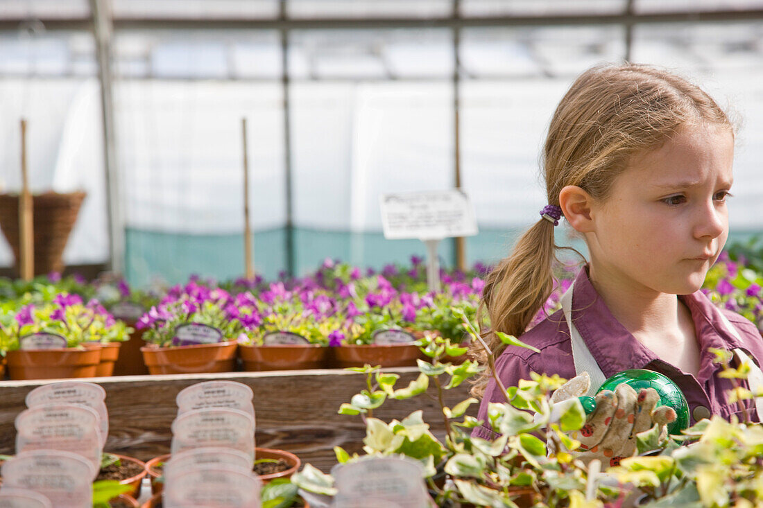 Portrait of young girl amongst flowerpots inside greenhouse\n