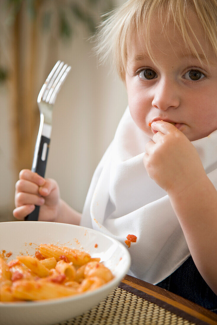 Portrait of young blonde boy eating pasta\n