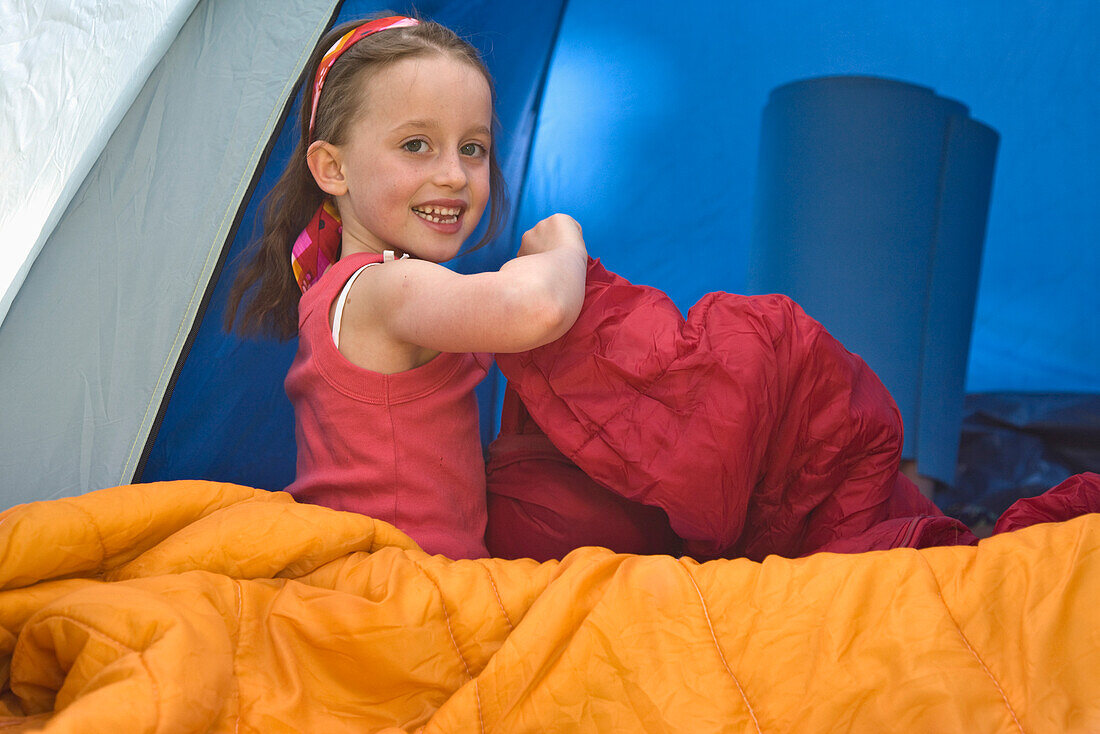Junges Mädchen sitzt in einem Zelt und öffnet einen Schlafsack