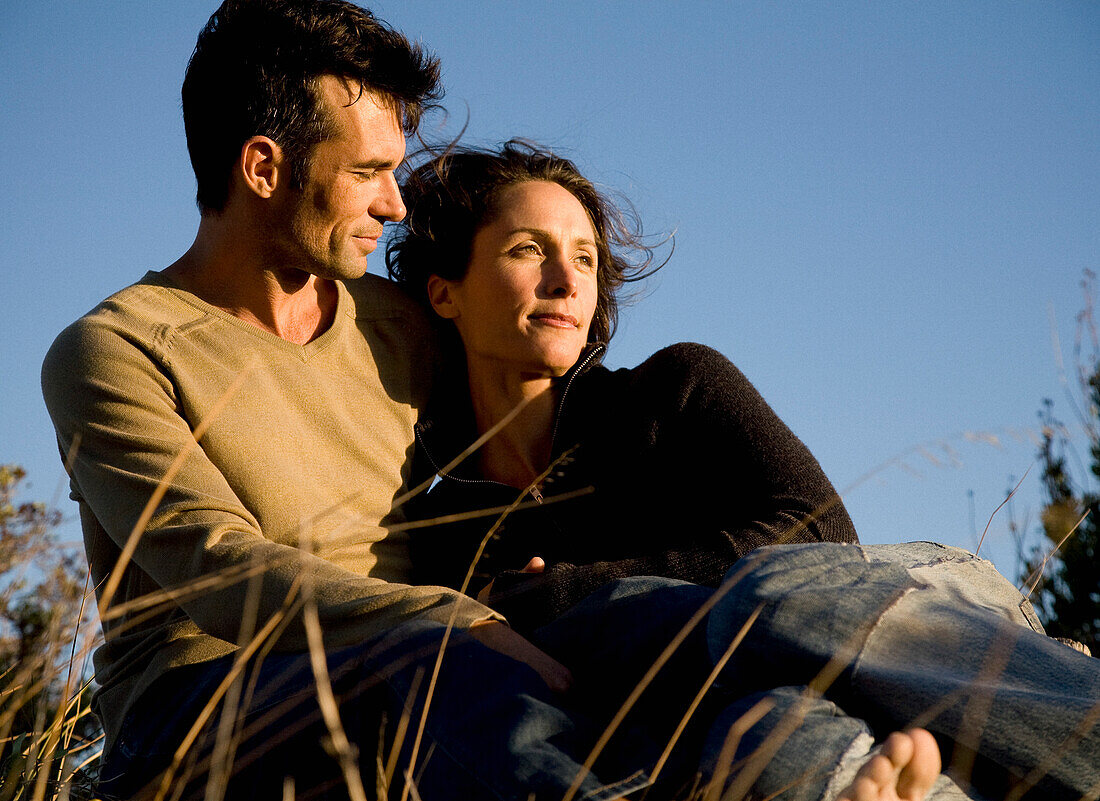 Portrait of couple embracing sitting on field\n