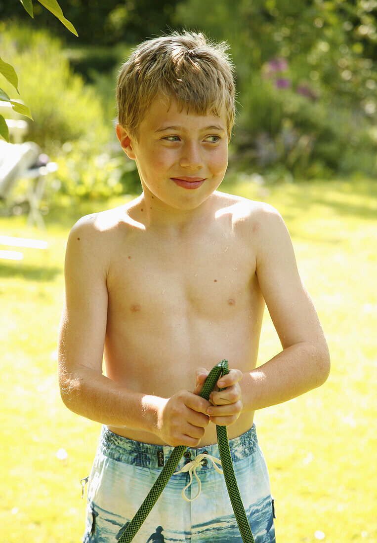 Junger Junge mit Gartenschlauch in der Hand