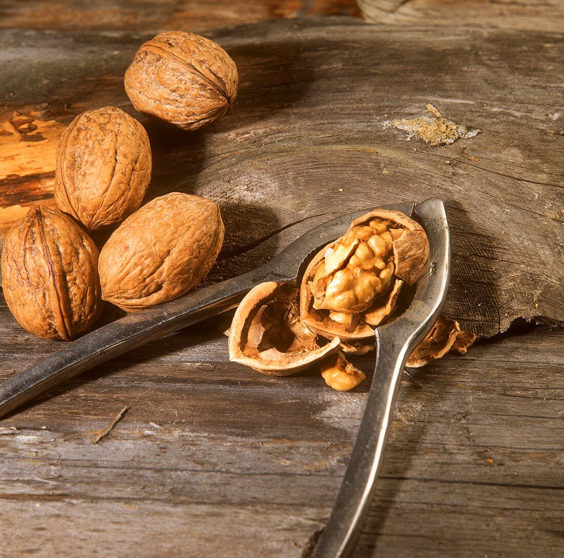 Walnuts, one opened with nutcracker, on wooden background