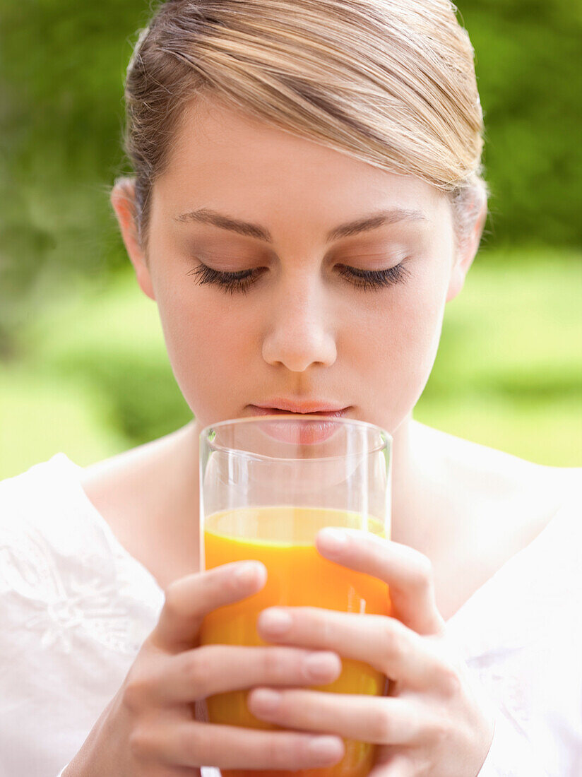 Close up of a young woman holding a glass of orange juice\n