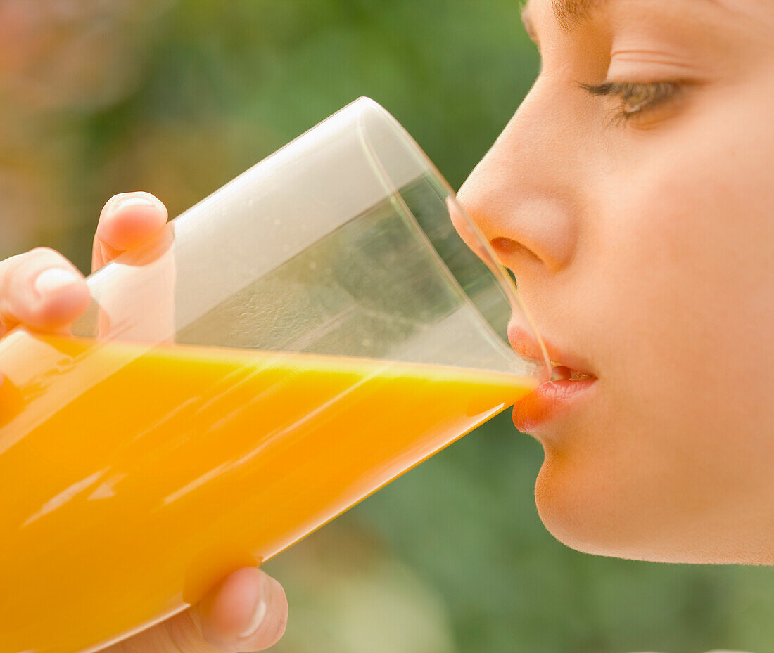 Close up of a young woman drinking and holding a glass of orange juice - profile\n