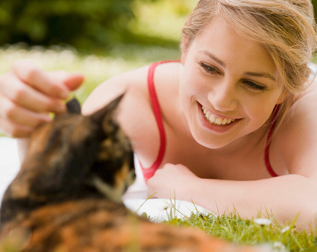 Young woman lying on the grass caressing a cat\n