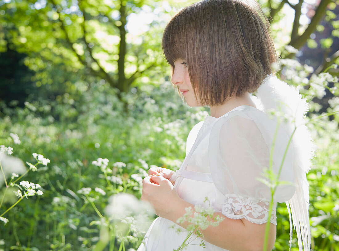 Portrait of young girl in a white fairy costume standing in a garden\n