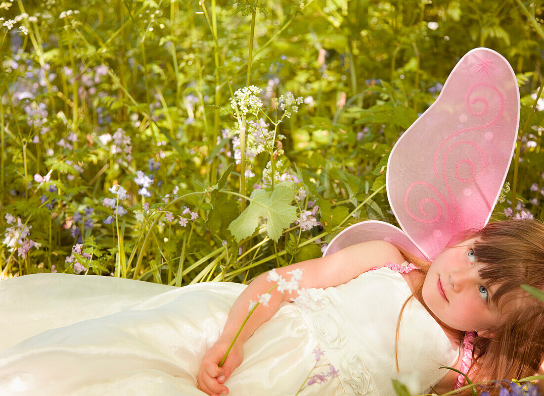 Porträt eines jungen Mädchens in einem Feenkostüm, das in einem Blumenfeld liegt
