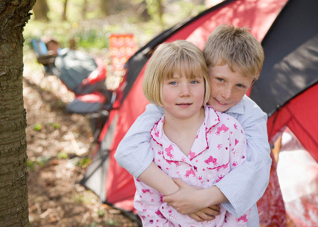 Porträt eines Jungen und eines Mädchens, die sich vor einem Zelt auf einem Campingplatz umarmen