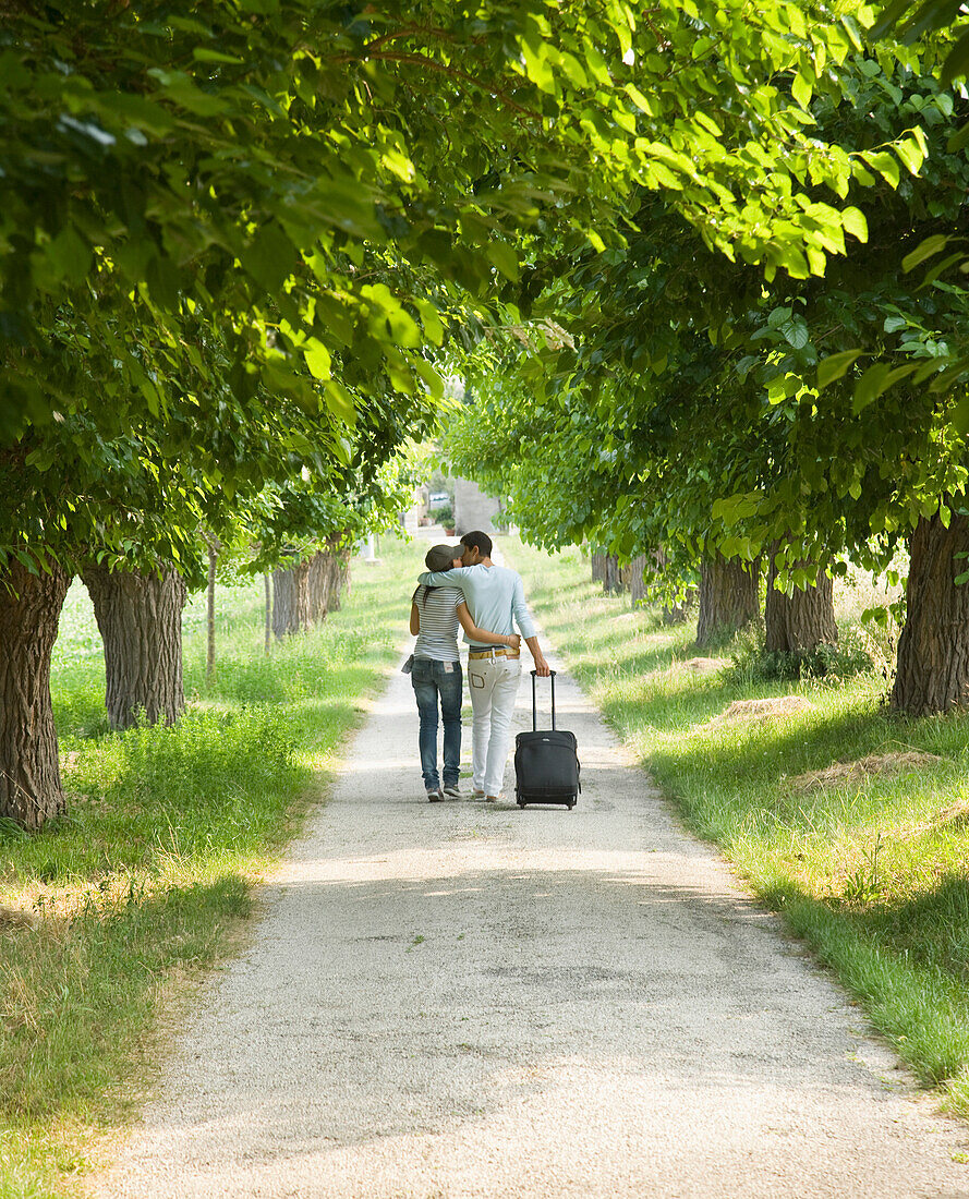 Junges Paar beim Spaziergang mit Koffer und küssend