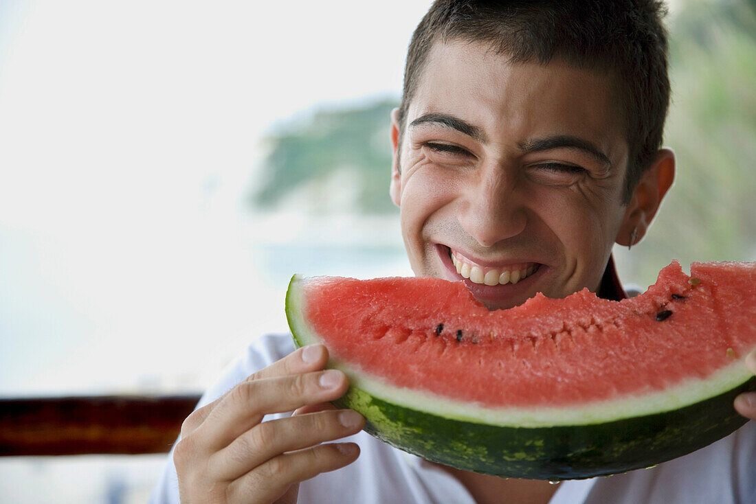 Junger Mann isst Wassermelone und lacht