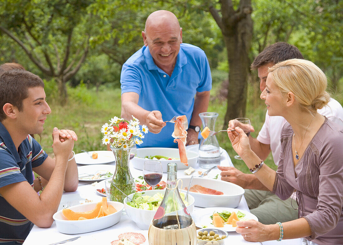 Bald granddad serving ham to family group\n