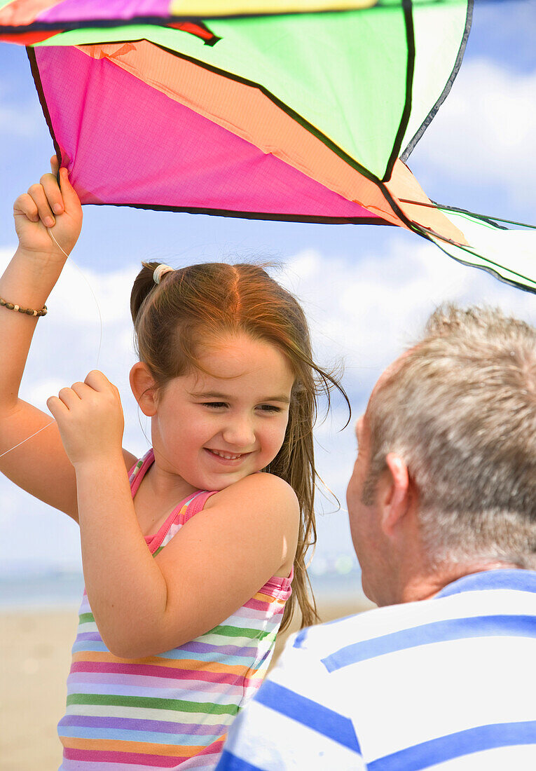 Young girl holding kite and smiling to her father\n