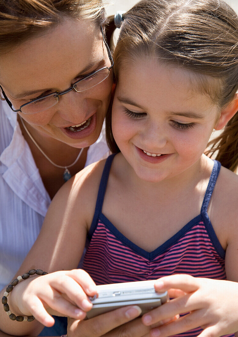 Mother and daughter holding digital camera looking at photos\n