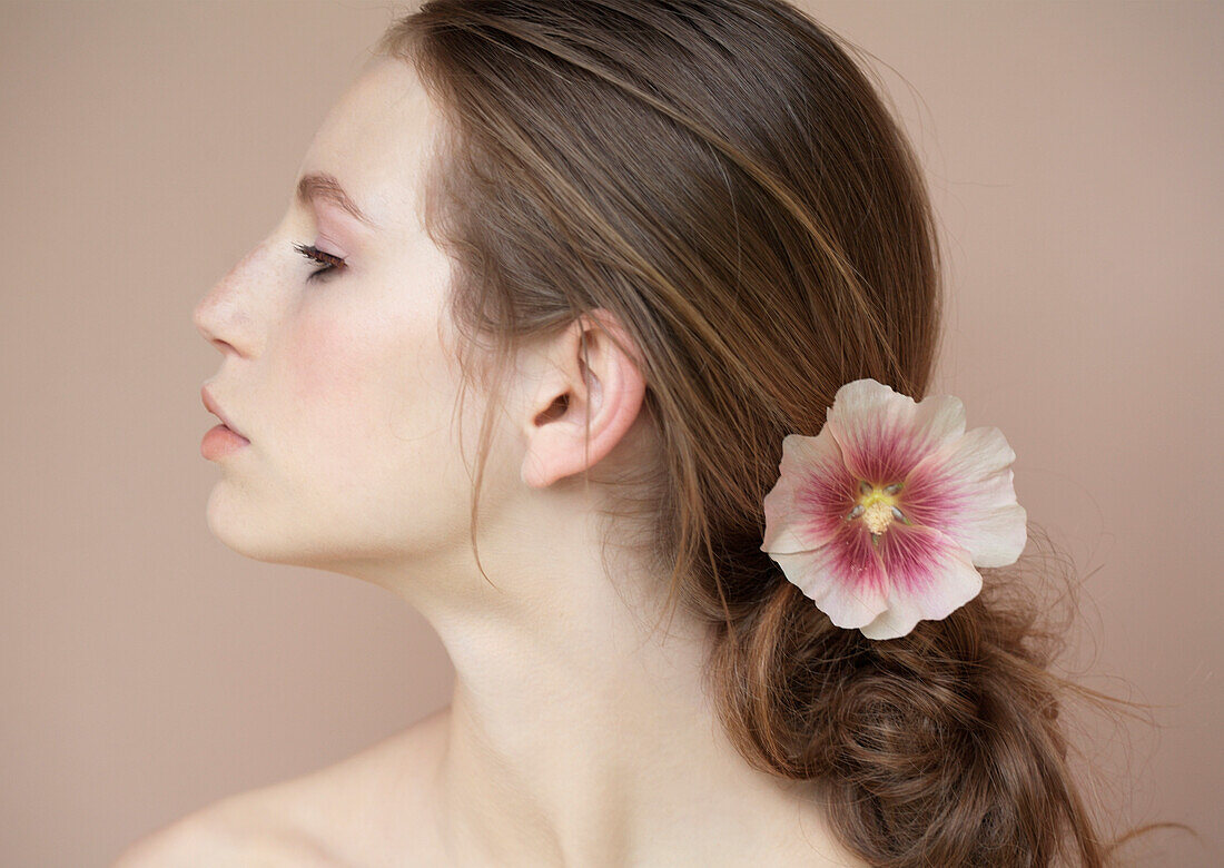 Profil einer schönen jungen Frau mit Blume, die ihr Haar zurückhält