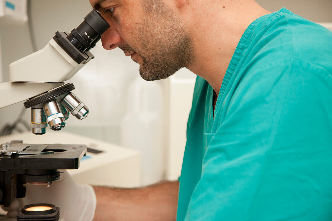 Lab technician looking into microscope\n