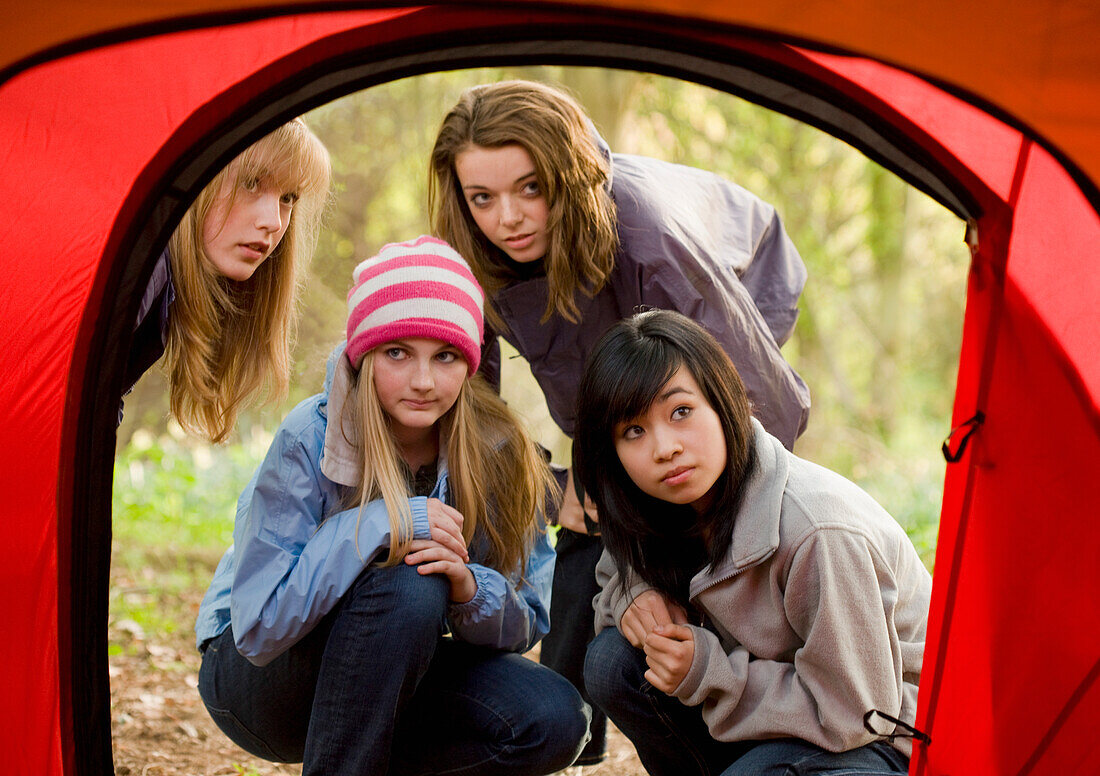 Mädchen im Teenageralter auf dem Campingplatz hockt vor dem Zelteingang und schaut neugierig hinein