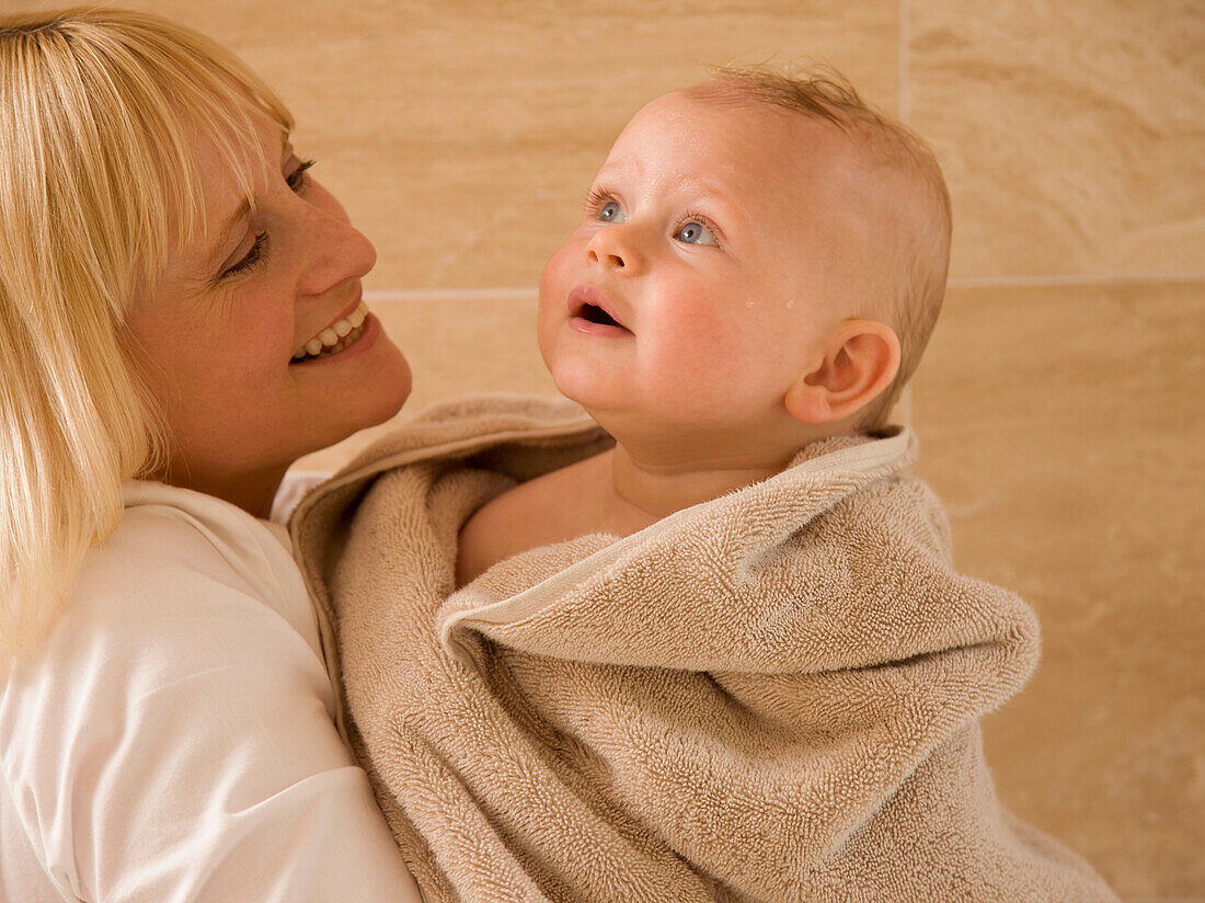Close up of baby wrapped in  a towel with his mother holding him\n