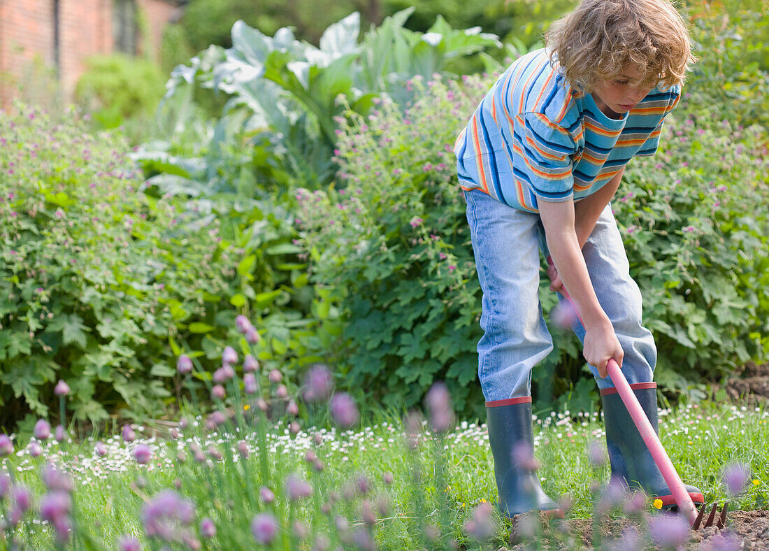 Junger Junge gräbt mit Hacke und Gabel im Garten