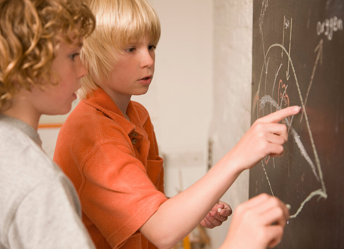 Two young boys writing on a blackboard\n