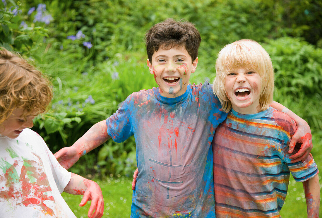 Junge Jungen mit Aquarellfarben bedeckt lachend in einem Garten