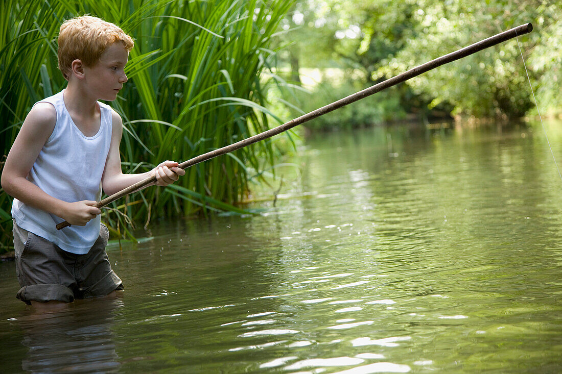Young boy fishing in a river with his legs in the water\n