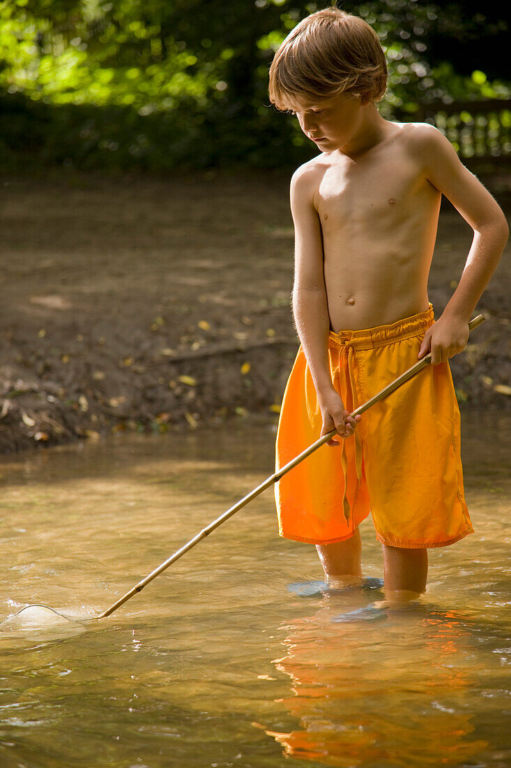 Young boy fishing in a river with fishing net\n