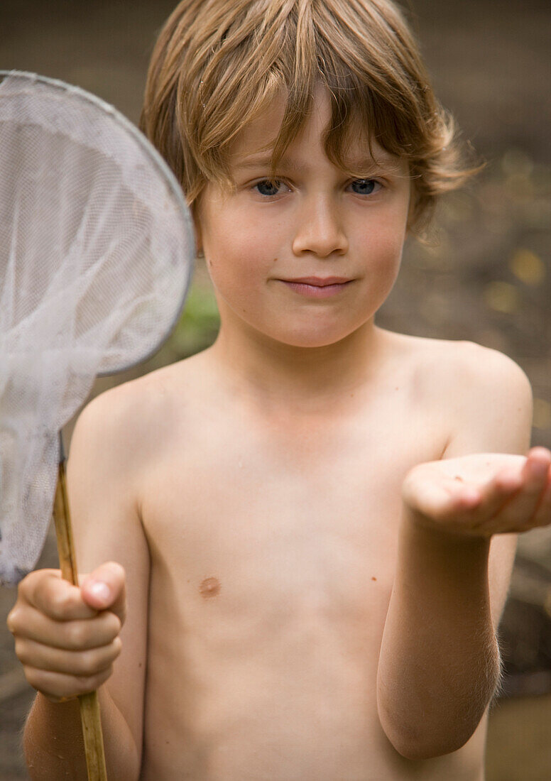 Young boy holding a fishing net with a tadpole on his hand\n