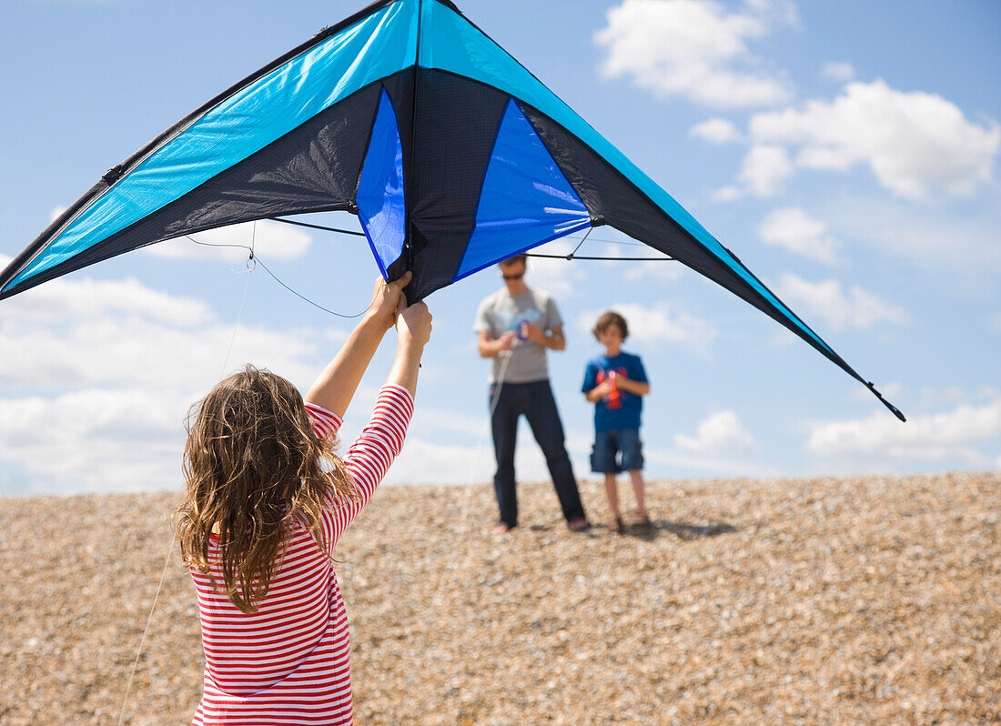 Back view of young girl standing on a beach holding a kite\n