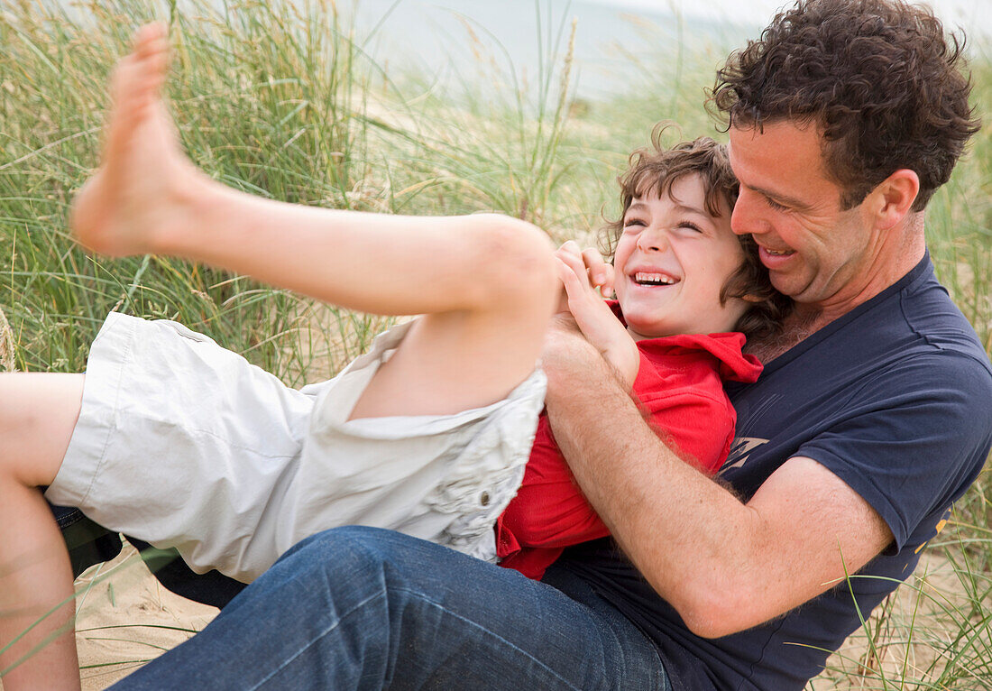 Vater und Sohn sitzen lächelnd und streitend am Strand