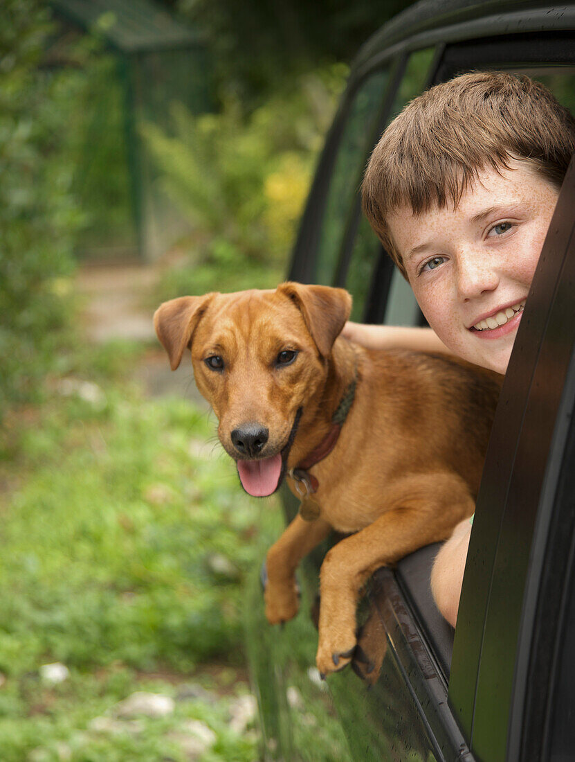 Young boy  and his dog leaning out of car window\n