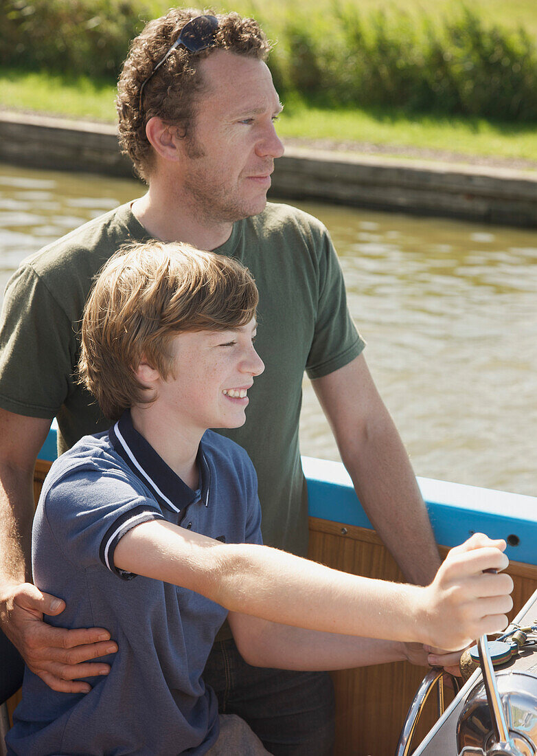 Man and smiling teenaged boy steering a boat\n