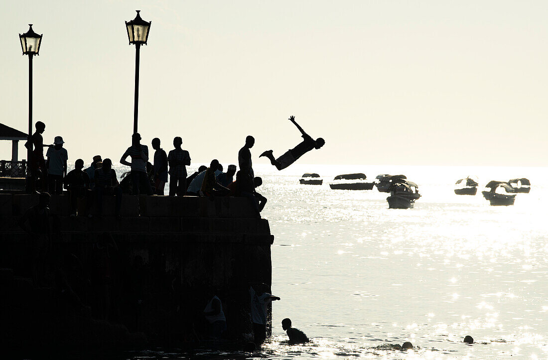 Silhouetted teenagers dive into the sea from the town pier, Stone Town, Zanzibar island, Tanzania, East Africa, Africa\n