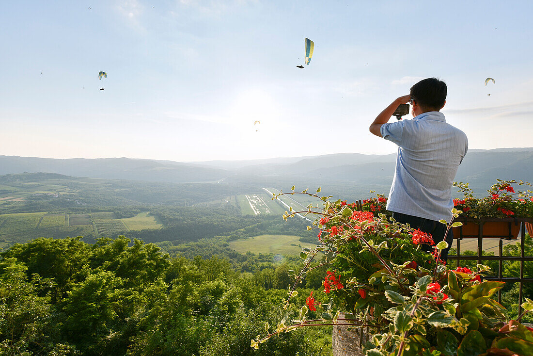 Ein Tourist fotografiert Gleitschirmflieger von der Spitze des Bergdorfes Motovun, Istrien, Kroatien, Europa