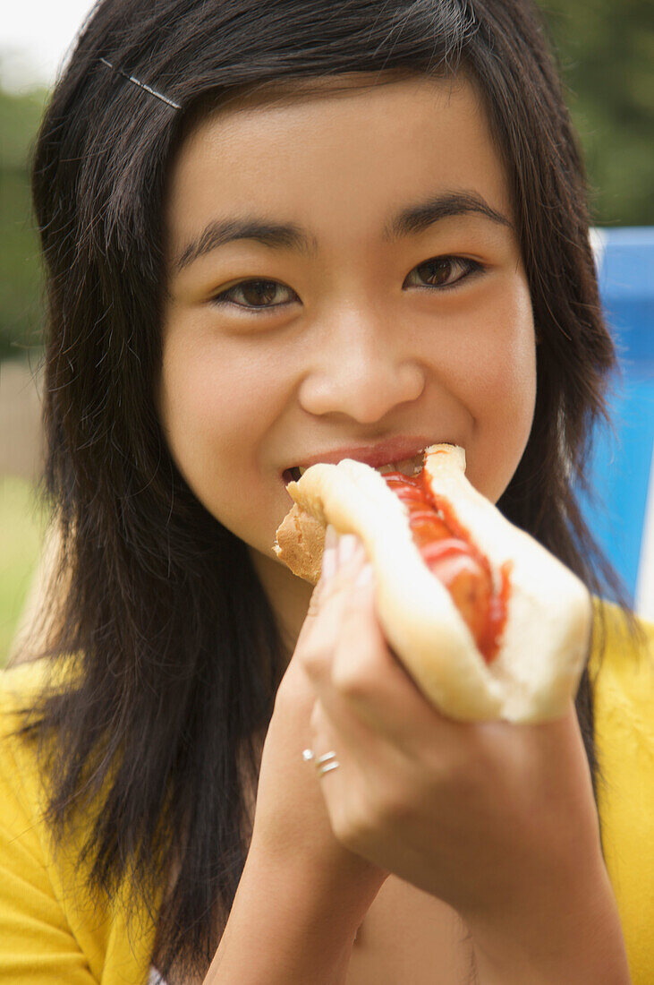 Close up of a teenaged girl eating a hot dog\n