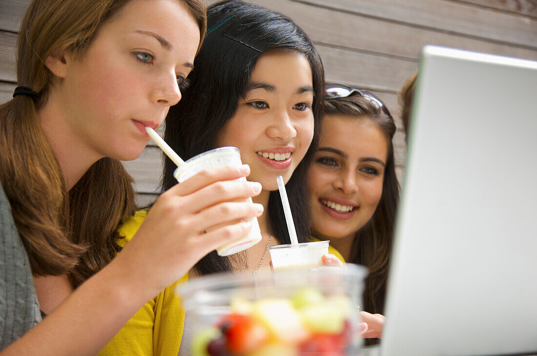 Mädchen im Teenageralter, die einen Laptop benutzen und einen Milchshake trinken