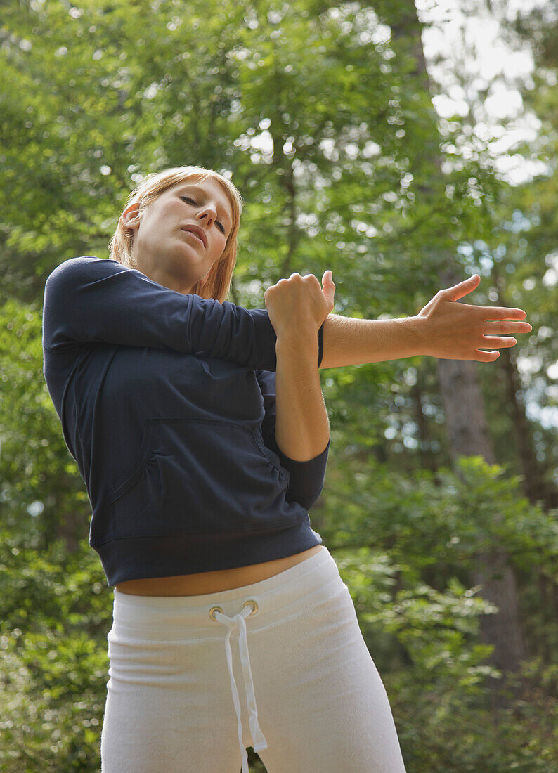 Young woman standing in a forest stretching her arm\n