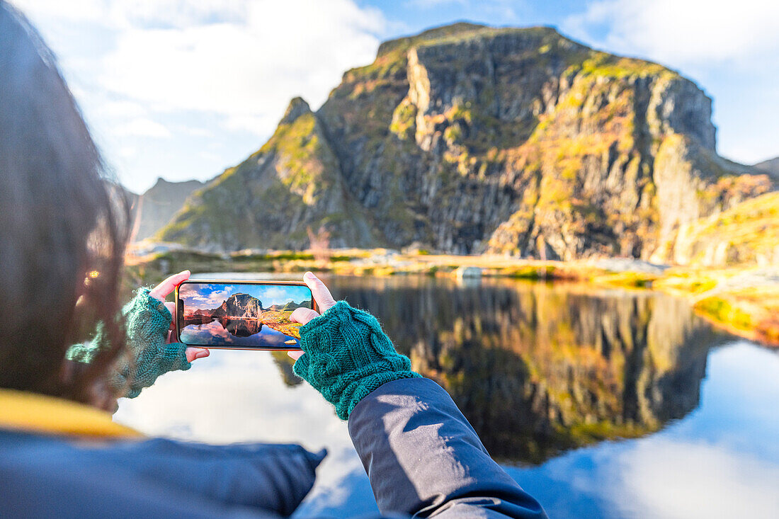 Personal perspective of woman photographing mountains in autumn with smartphone, A i Lofoten, Moskenes, Lofoten Islands, Nordland, Norway, Scandinavia, Europe\n