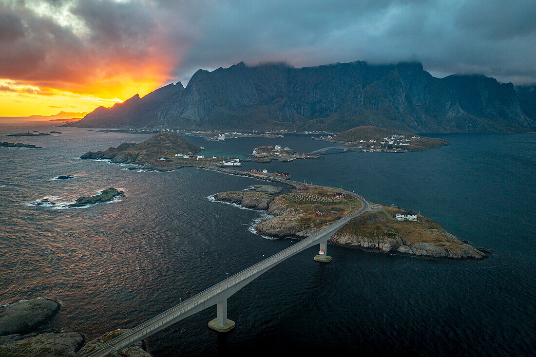 Luftaufnahme einer Brücke über den Fjord unter einem dramatischen Himmel bei Sonnenuntergang, Reine Bucht, Lofoten Inseln, Nordland, Norwegen, Skandinavien, Europa